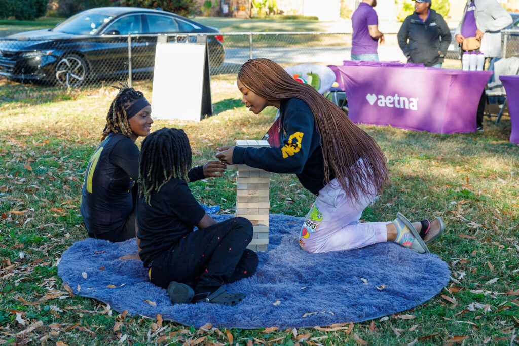 Three young people playing Jenga in front of a Aetna table at the Aetna Virginia Thanksgiving Pop-Up Grocery Market