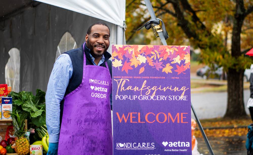 Andre Greenwood from Aetna poses with the purple welcome sign at the Kandi Cares and Aetna Thanksgiving Pop-Up Grocery Market