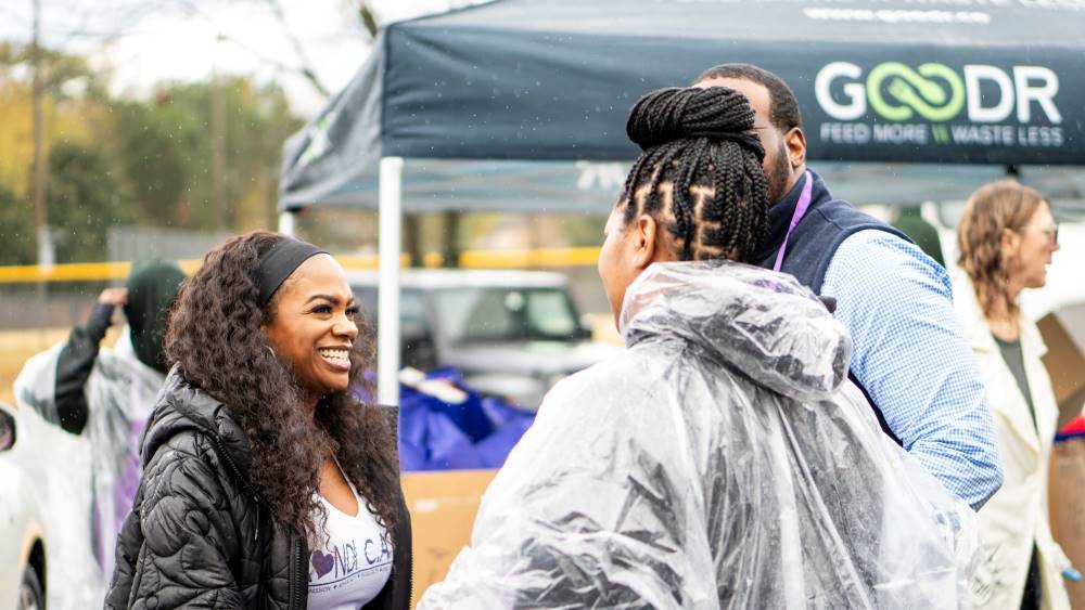 Kandi Burruss talking to Goodr and Aetna team members in front of a Goodr tent