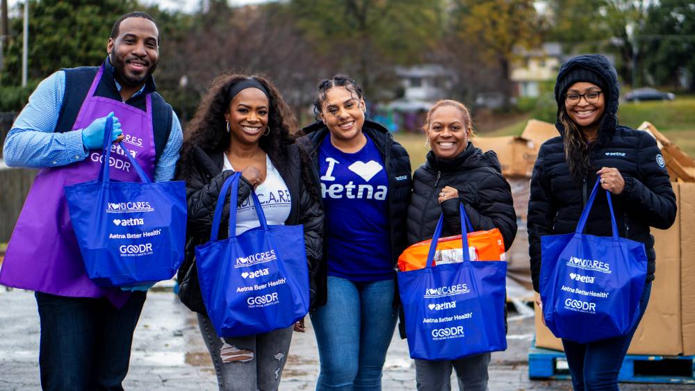 Kandi Burruss and a group of Aetna team members holding bags of free shelf-stable groceries