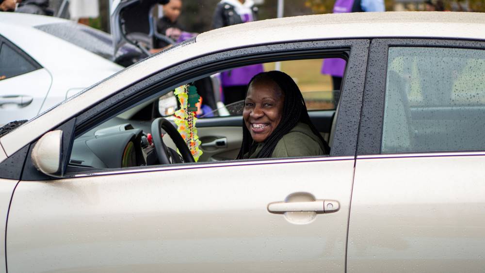 A woman with braids smiles in her tan car at the Kandi Cares and Aetna Thanksgiving Pop-Up Grocery Market
