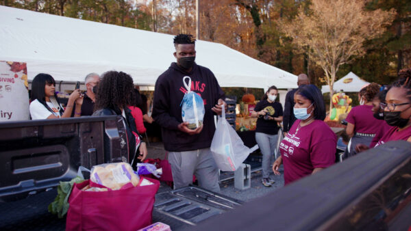 Atlanta Hawks star Clint Capela placing a turkey and groceries in the back of an attendee's car at the Goodr Pop-Up Market