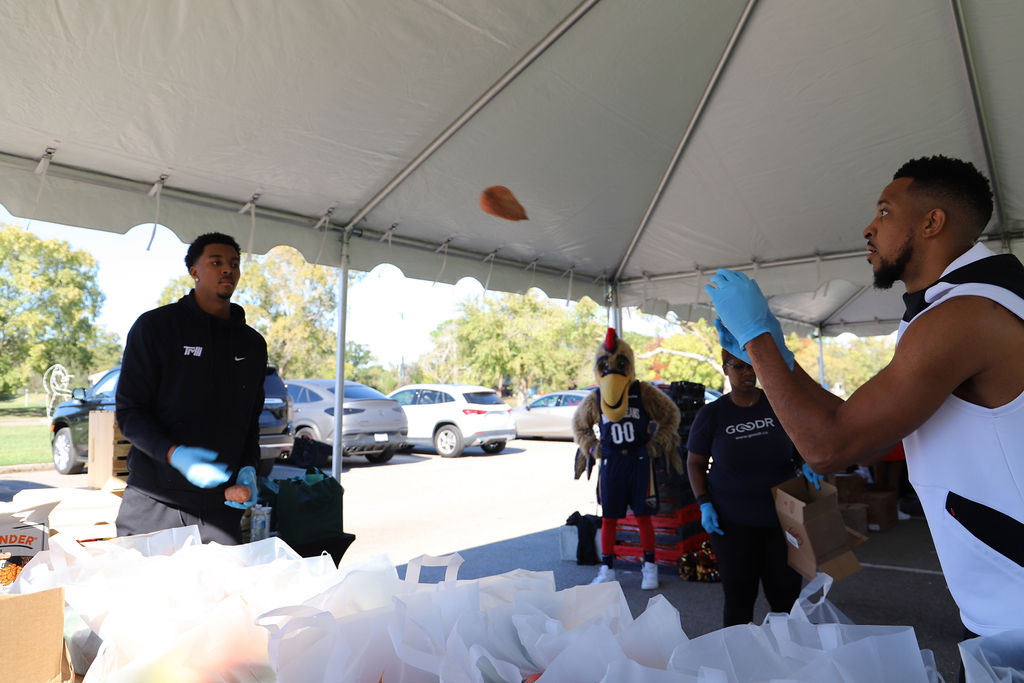 New Orleans Pelicans players CJ McCollum and Trey Murphy III pass a sweet potato to load into clear plastic produce bags at CJ McCollum's McCollum Friendsgiving 2023