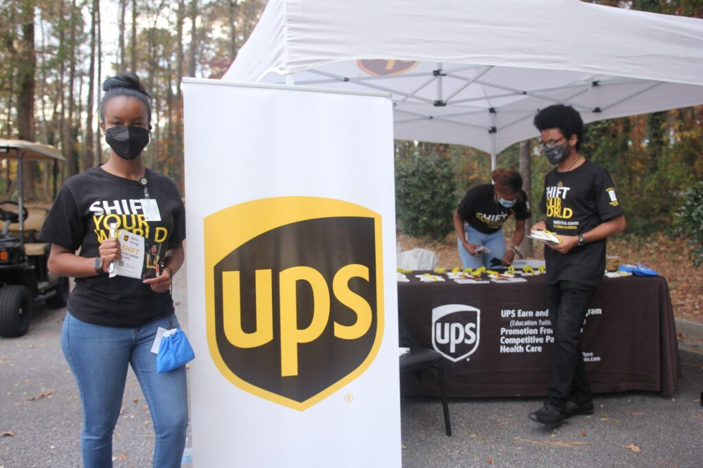 Three members of the UPS corporate team at a table ready to discuss job opportunities with UPS at the Atlanta Hawks Thanksgiving Pop-Up Grocery Market.